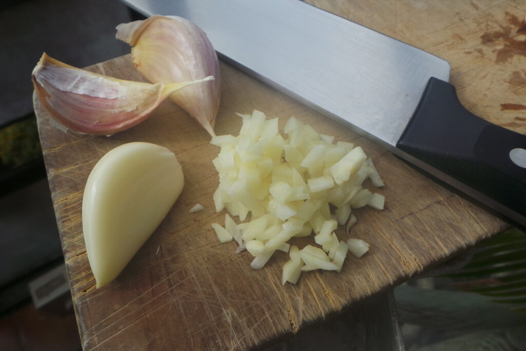 Large garlic cloves being chopped on a cutting board